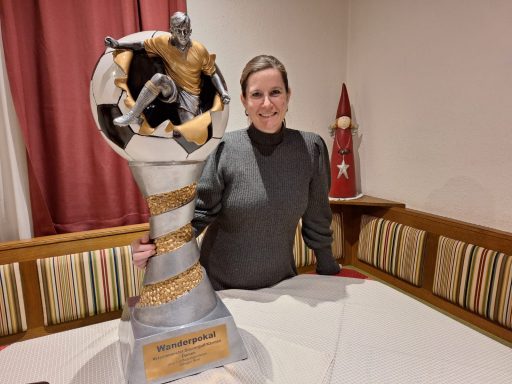 Frau mit einer großen, silbernen Trophäe steht an einem Tisch.